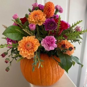 Floral arrangement of red, orange and pink flowers using a small pumpkin as a vase.