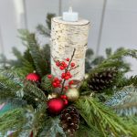 birch candle surrounded by evergreens and red berries